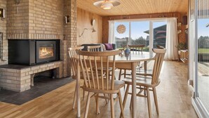 Ein gemütliches Zimmer mit Kamin, Holzbalkendecke und Essecke mit Stühlen und Tisch.