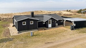 Ein schwarzes Gebäude aus Metall mit flachem Dach, einem überdachten Außenbereich und Blick auf das Meer.