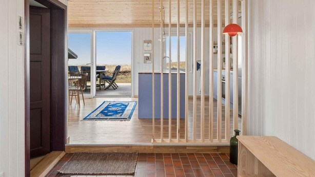 Ein Zimmer mit Holzboden, einer Schiebetür zu einem Außenbereich, einer Küchenzeile und einem Esstisch mit Stühlen.