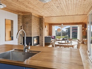 A modern kitchen with a brick fireplace, wooden ceiling, and a dining area with a view. - 4 Star Holiday Home in Spottrup (Spøttrup)