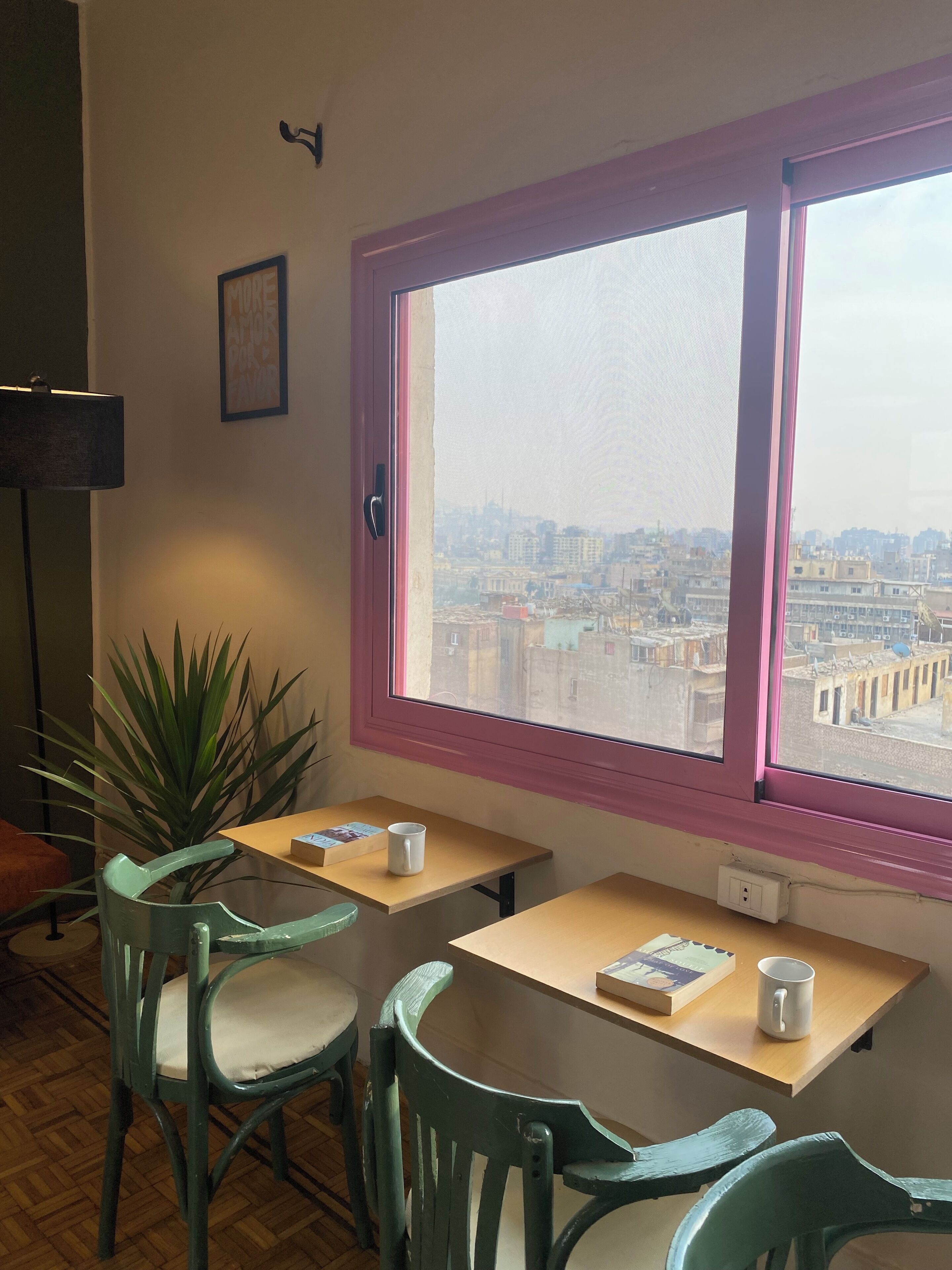 Una habitación con dos mesas, dos sillas, una planta en maceta y una ventana que da a vistas de la ciudad.
