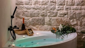 A spa area with a stone wall, a bathtub, candles, a bottle, and a wooden box.