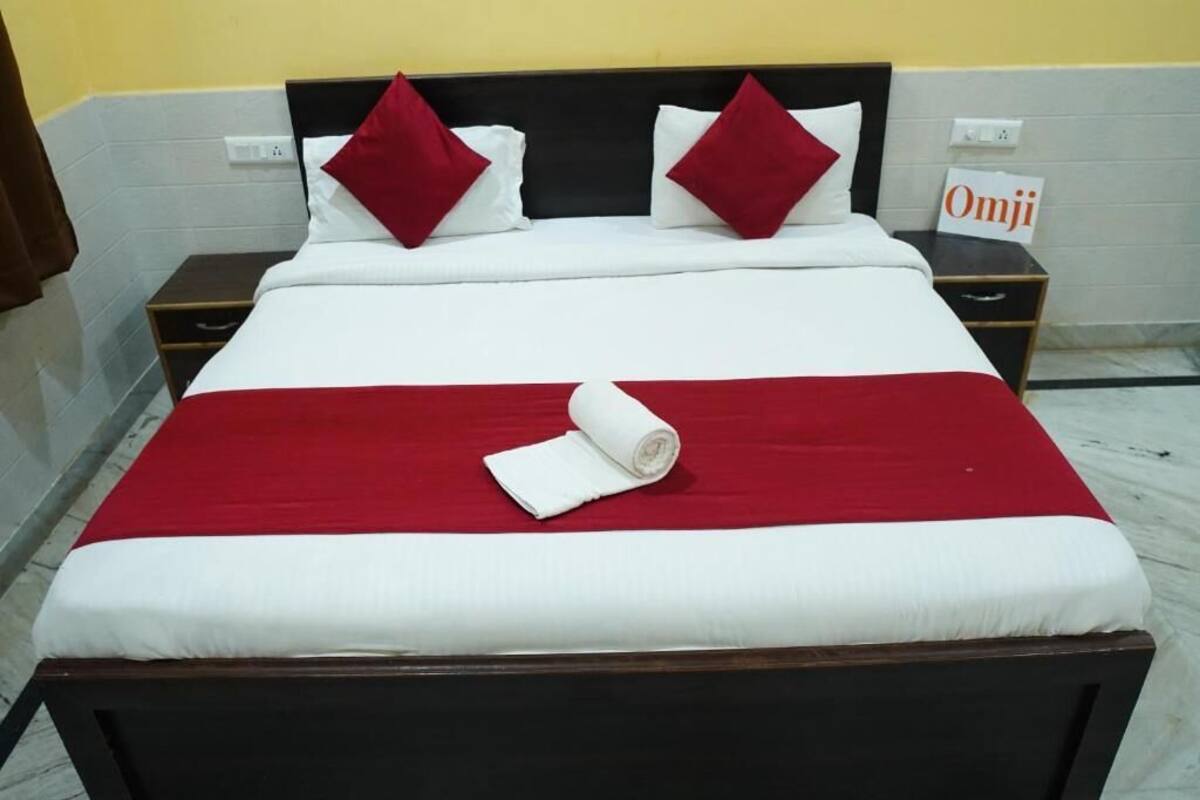 A neatly made bed with a red and white bedspread, two red pillows, and a rolled white towel.