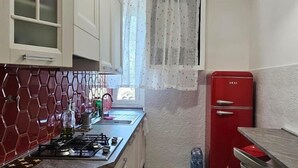 Una cocina con armarios blancos, un refrigerador rojo, una estufa a gas y un ventilador de techo.