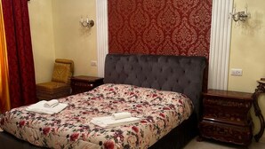 Un dormitorio con una cama grande, una araña, una pared con estampado rojo y una mesita de noche de madera.