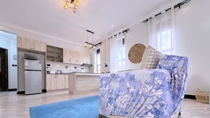 A modern bedroom with a bed, a blue rug, and a kitchen in the background. - Constatia Homes (Kampala)