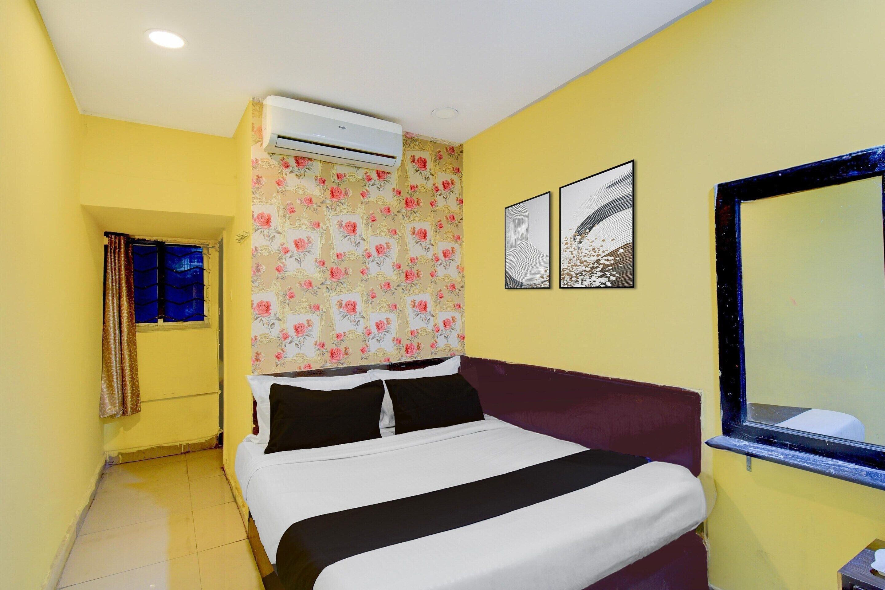 A hotel room with a bed, air conditioning unit, floral wallpaper, two framed artworks, and a window with a view.