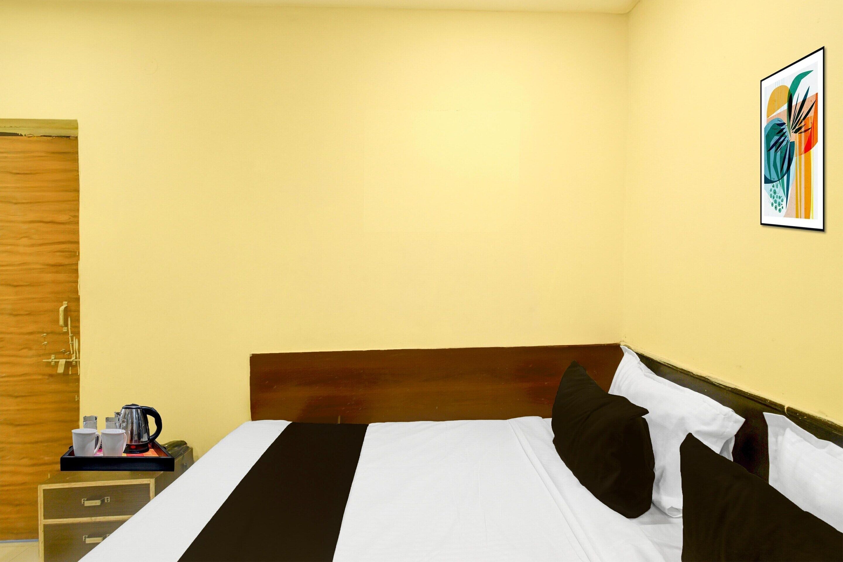 A hotel room with a bed, a nightstand, a tray with a kettle, cups, and a plate, and a wooden door.