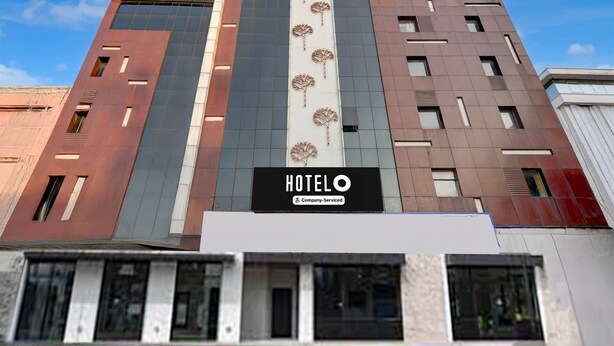 Un moderno edificio de hotel con un llamativo letrero 'HOTEL', diseño vertical con motivos de árboles y un cielo despejado al fondo.