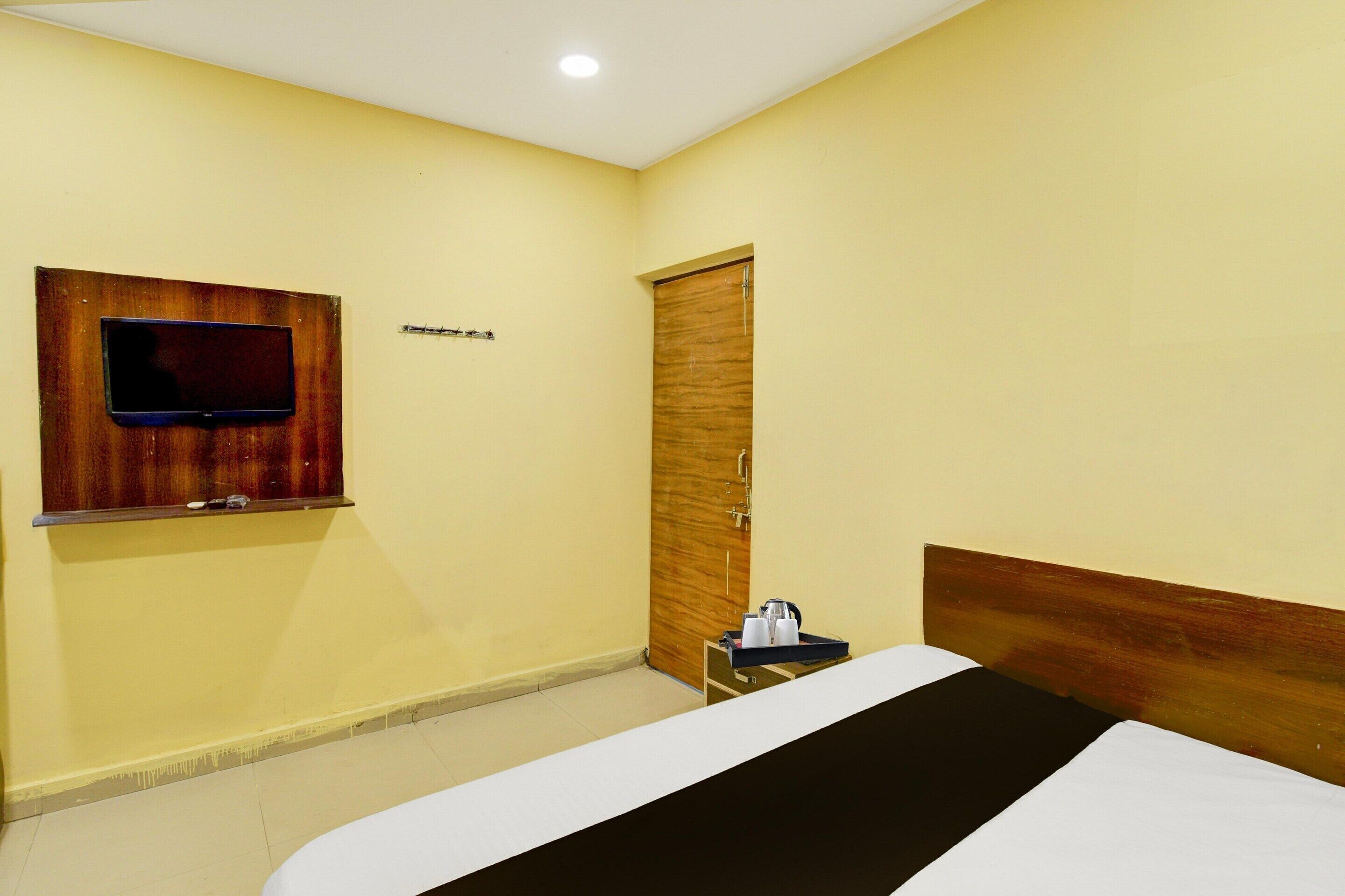 Una habitació d'hotel amb un llit, una televisió penjada a la paret, una porta de fusta i una taula petita amb una safata.