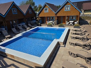Ein Schwimmbad mit Liegestühlen und Holzbungalows.