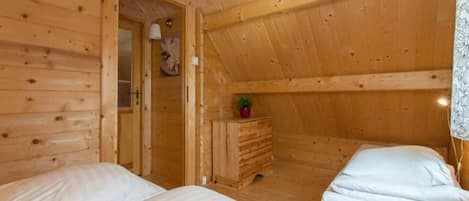 A wooden cabin with two beds, a dresser, and a ceiling light.