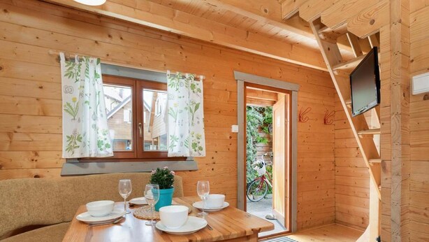 Un interno in legno con un tavolo da pranzo apparecchiato per due, un divano, una pianta in vaso e un televisore montato a parete.