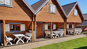 Une rangée de cabanes en bois, dotées d’espaces extérieurs pour s’asseoir, et un chemin pavé de briques.