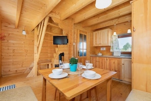 Ein Holzblock-Interieur mit einem Esstisch, der für vier Personen gedeckt ist, einem an der Wand montierten Fernseher und einer Küchenzeile mit Holzschränken.