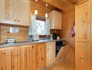 A wooden kitchen with a built-in dishwasher, a stove, and a window with floral curtains. - Two-story Holiday Homes With a Pool (Rewal)