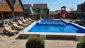 Une piscine entourée de bâtiments, avec des chaises longues et un toboggan.