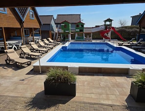 A swimming pool with lounge chairs and a slide, surrounded by buildings. - Two-story Holiday Homes With a Pool (Rewal)