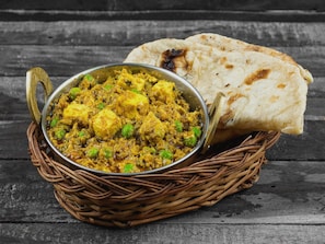 A dish of paneer curry with naan bread on a rustic wooden table.