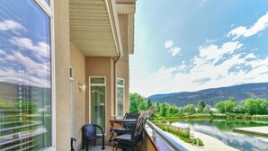 Een balkon met tafel en stoelen, met uitzicht op een rivier en groen.