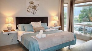 Een slaapkamer met een bed, twee bedlampen, een raam met uitzicht op boten, en een schilderij aan de muur.