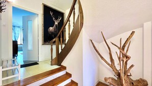 A staircase with wooden steps and a wooden handrail, leading to a room with a framed deer head painting.