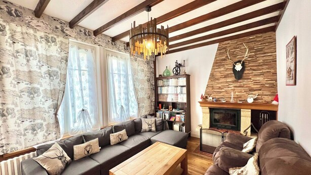 A cozy living room with a fireplace, a wooden ceiling, and a bookshelf.