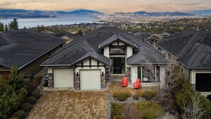 A residential area with houses, a driveway, and a view of mountains and a body of water. - Bright open-concept home in Kelowna with lake views, high ceilings, fireplace. (Kelowna)