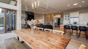 A modern kitchen with white cabinets, a wooden dining table, and a geometric pendant light. - Bright open-concept home in Kelowna with lake views, high ceilings, fireplace. (Kelowna)