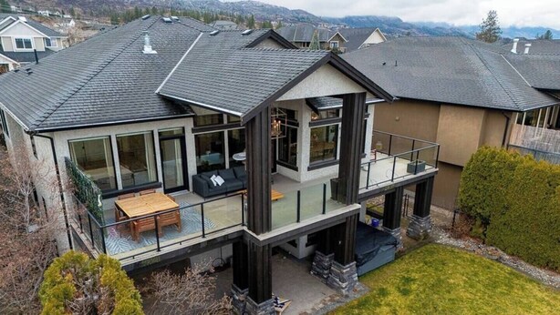 A modern two-story house with a balcony, large windows, and a stone foundation. - Bright open-concept home in Kelowna with lake views, high ceilings, fireplace. (Kelowna)