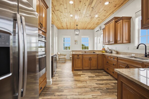 A kitchen with wooden cabinets, a stainless steel refrigerator, a wooden ceiling, and a herringbone floor pattern.
