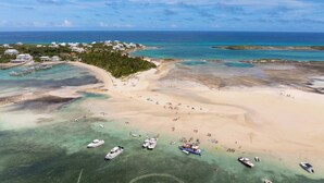 An aerial view of a beach with boats, a clear blue sea, and buildings in the background. - Turtle Cay Bahamas🤿Blue Marlin🛥️Marina (Green Turtle Cay)