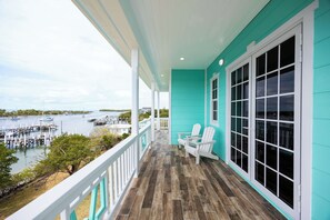 A covered porch with a view of a dock and boats, white chairs, and a turquoise building.