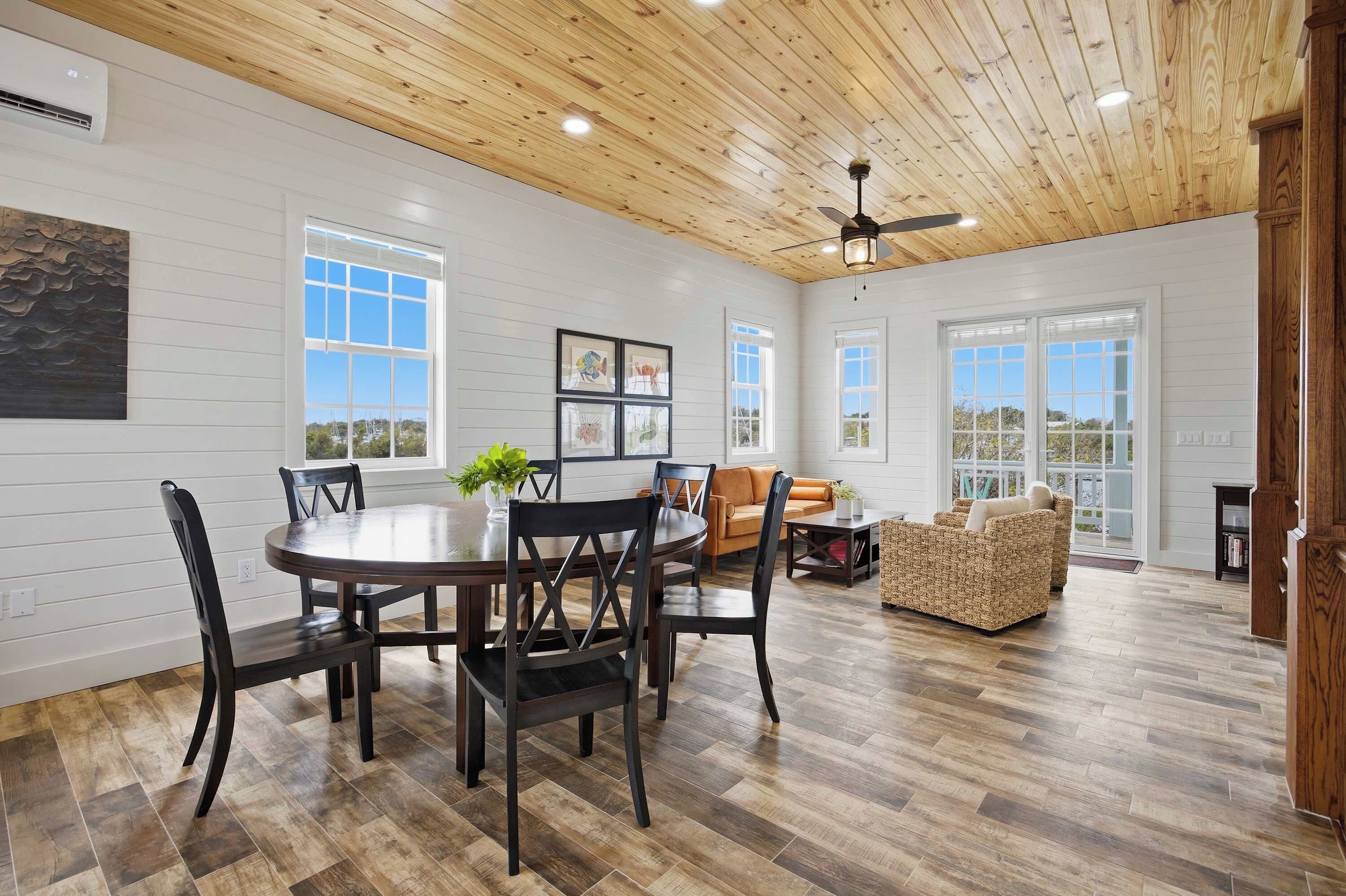 A spacious room with a wooden ceiling, a dining table with chairs, a sofa, and a wicker loveseat.