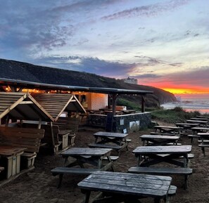 Ein Restaurant direkt am Strand mit Außenbereich und Blick auf den Sonnenuntergang über dem Meer.