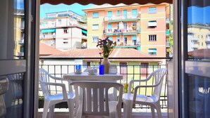 Ein Balkon mit Tisch und Stühlen, einer Blumenvase und Blick auf mehrstöckige Gebäude.