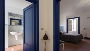 Camera da letto con un letto, un comodino, una finestra e un bagno con lavandino e specchio.