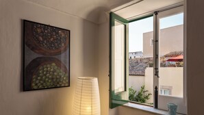 Una stanza con una finestra, un quadro appeso al muro e una lampada alta e cilindrica.
