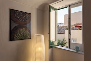 Ein Zimmer mit Fenster, einem Wandbild und einer hohen, zylindrischen Lampe.