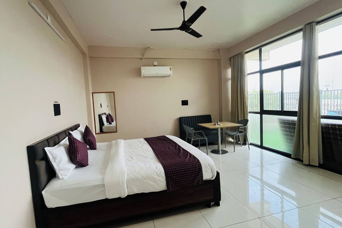 Habitación de hotel con cama, ventilador de techo, mesa con sillas, ventana con vistas y equipo de aire acondicionado.