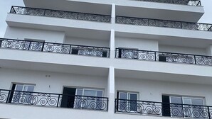 A multi-story building with balconies, a garage entrance, and a door with a circular emblem. - Bazaj Residence (Sarande)