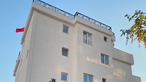 A multi-story building with a white facade, a balcony with black railings, and a flag on the left side. - Bazaj Residence (Sarande)