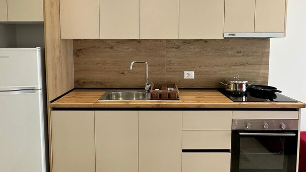 A modern kitchen with a stainless steel sink, wooden countertop, and a built-in oven. - Bazaj Residence (Sarande)