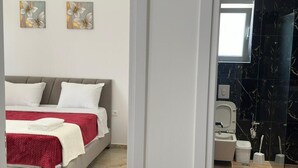 A bedroom with a bed, two pillows, a red blanket, and two wall art pieces. - Bazaj Residence (Sarande)