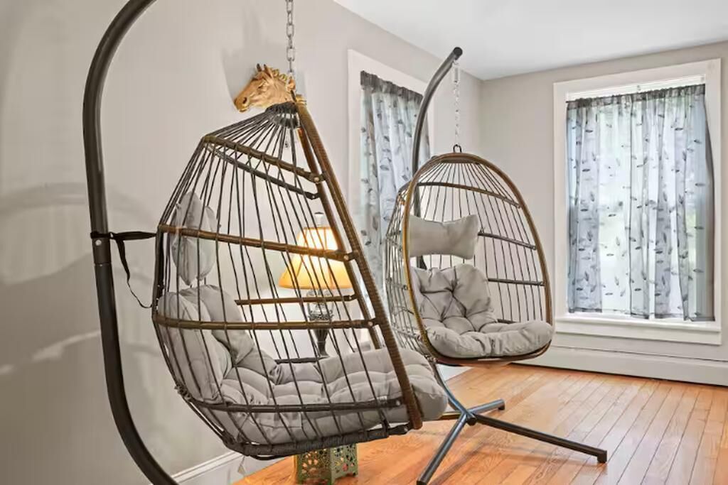 A room with two hanging chairs, one with a horse head decoration, and a cushioned chair.