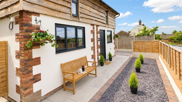 A wooden house with a bench, potted plants, and a gravel pathway. - Sleeps 2 in a quiet village location with hot tub and garden (Cotehill)