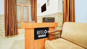 A hotel reception desk with a sign indicating it is company-serviced. There is a sofa and a window with curtains. - Deluxe Dream Stay Hotel (Lucknow)
