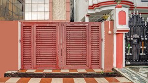 A gated entrance with a red door, a tiled pavement, and a building with a white and red facade in the background. - Deluxe Dream Stay Hotel (Lucknow)