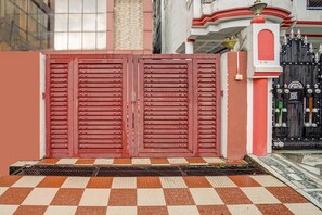 A gated entrance with a red door, a tiled pavement, and a building with a white and red facade in the background. - Deluxe Dream Stay Hotel (Lucknow)