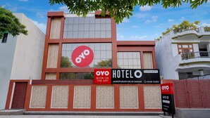 A hotel with a prominent red and white facade, a large OYO logo, and a sign indicating it's a company-serviced hotel. - Deluxe Dream Stay Hotel (Lucknow)